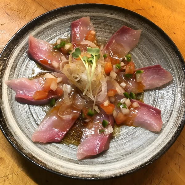 Japanese sashimi dish with thinly sliced fish, diced vegetables, and sprouts on a round plate.