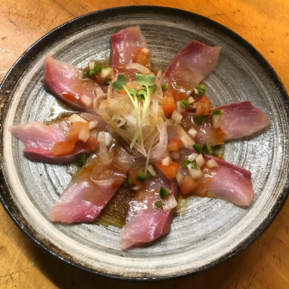 Japanese sashimi dish with thinly sliced fish, diced vegetables, and sprouts on a round plate.