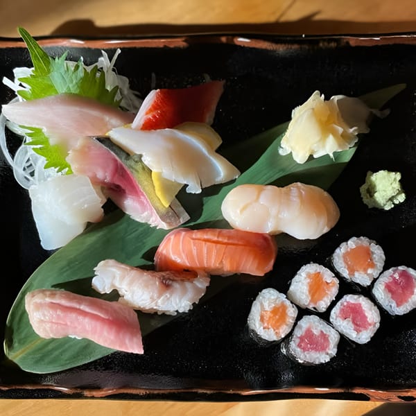 A black plate filled with various sushi and sashimi, including salmon, tuna, and scallops.