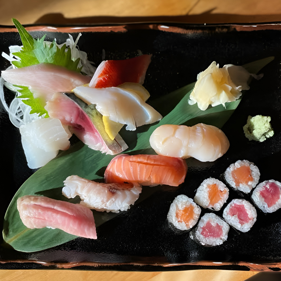 A black plate filled with various sushi and sashimi, including salmon, tuna, and scallops.