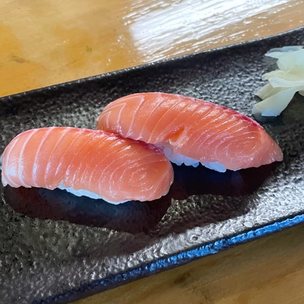 Two pieces of fresh tuna nigiri sushi with pickled ginger on a dark textured plate.