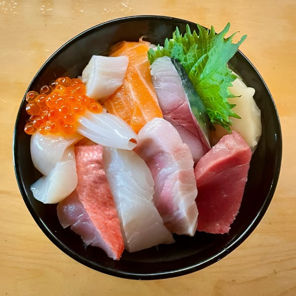 A colorful Japanese chirashi bowl with various sashimi, including salmon, tuna, squid, and roe.